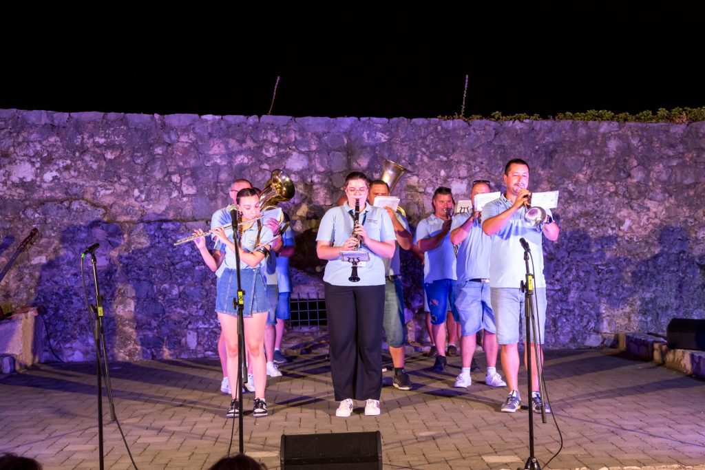 Nighttime outdoor brass band performing in front of a stone wall, musicians reading sheet music.