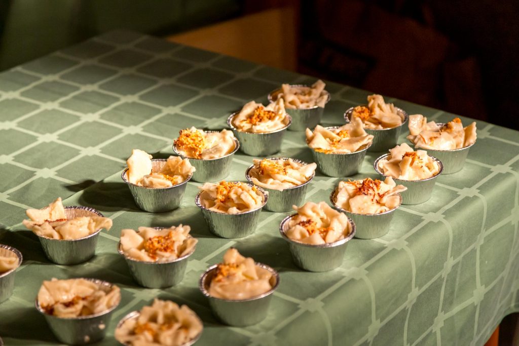 Several small aluminum dessert cups arranged on a green checkered tablecloth, each with piped frosting and crunchy topping.",