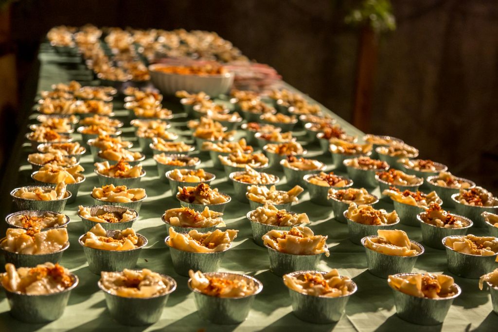 Row of small savory pastries in aluminum cups arranged on a long table at a banquet or tasting event.