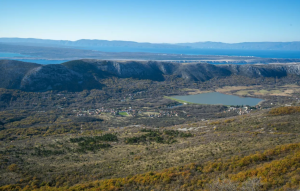 Expansive landscape with rolling hills, a lake in the midground, and distant blue mountains under a clear sky.