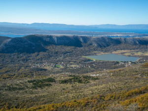 Expansive landscape with rolling hills, a lake in the midground, and distant blue mountains under a clear sky.