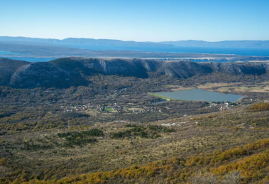 Expansive landscape with rolling hills, a lake in the midground, and distant blue mountains under a clear sky.